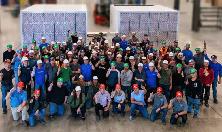 Photo of a large group of people wearing hard hats inside a manufacturing plant.