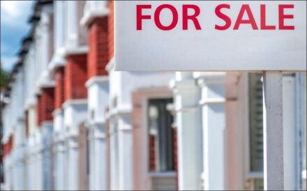 Photo of a For Sale sign in front of a row of condominiums.