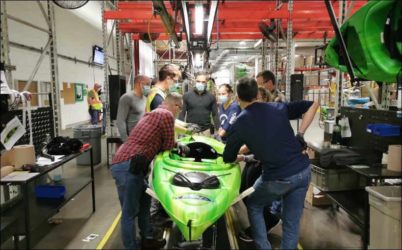 Photo of workers making a kayak inside a manufacturing plant.