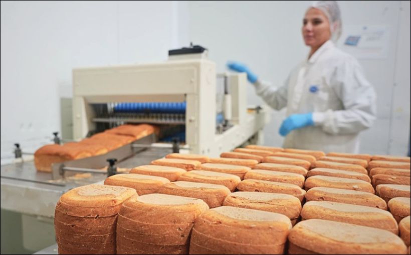 Photo of a female worker watching bread come out of an oven.