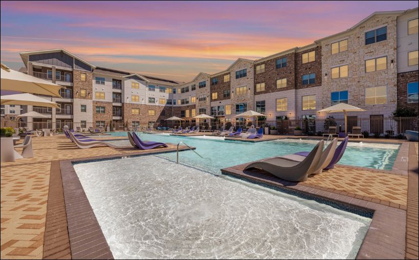 Photo of an apartment complex with a pool in front of it.