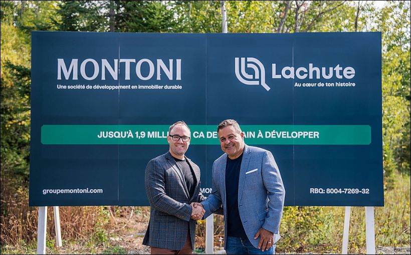 Photo of two men sharking hands in front of a large sign.