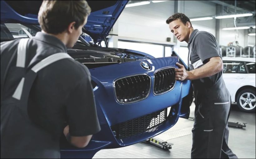 Two men work on a car in an autobody shop.